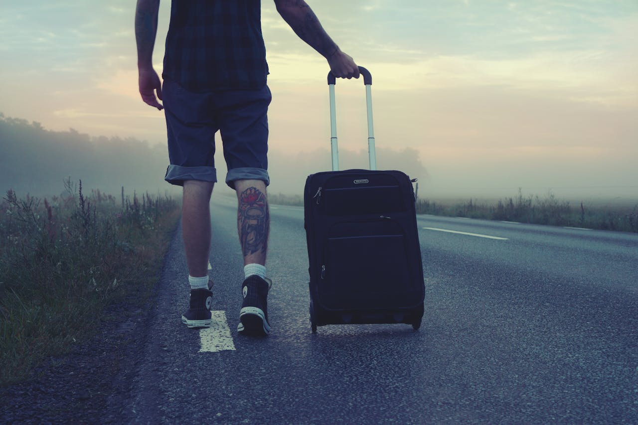 our-services-02 Man walking with a suitcase along a foggy road at sunrise, symbolizing adventure and travel.