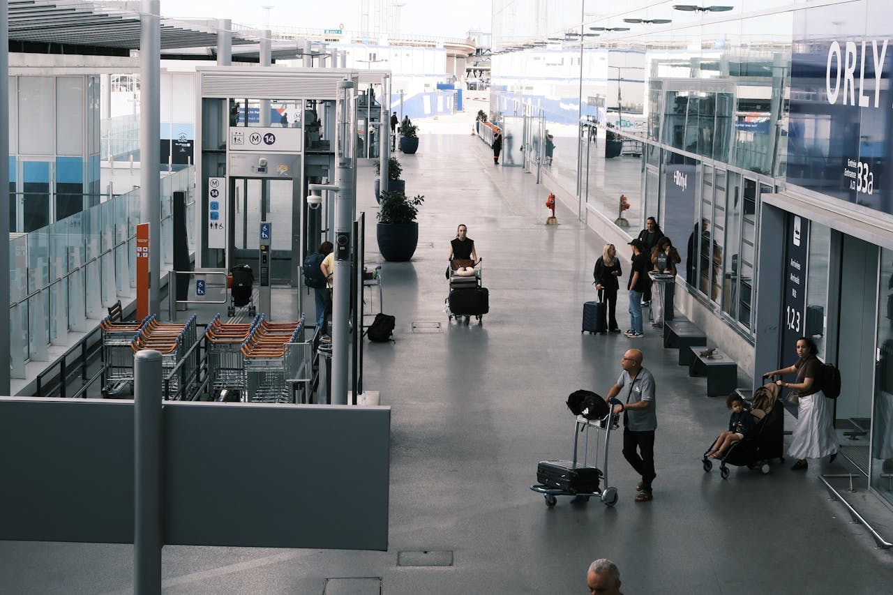 our-services-01 Travelers navigate an airport terminal corridor with luggage carts and suitcases.