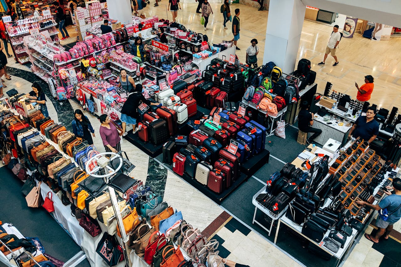 about-us-02 Overhead view of a vibrant shopping area in a Bangkok mall featuring purses, suitcases, and bustling shoppers.